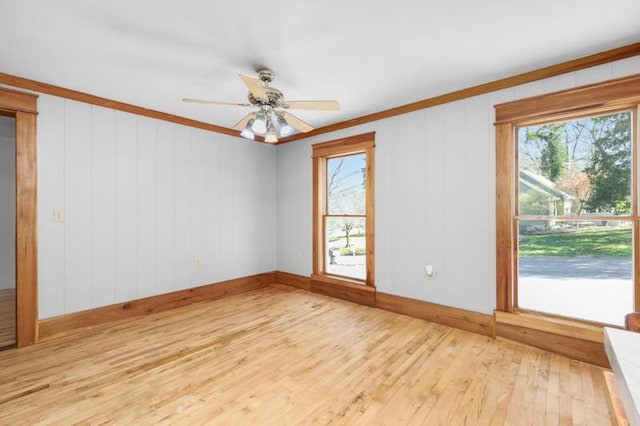 spare room with crown molding, light wood-style flooring, baseboards, and ceiling fan