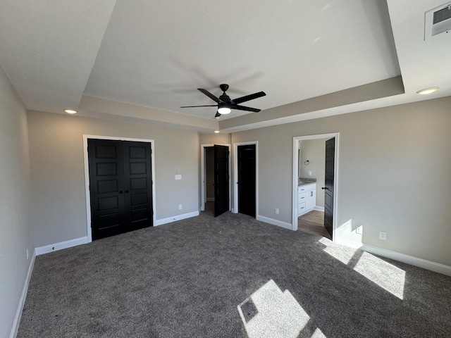 unfurnished bedroom with a tray ceiling, visible vents, baseboards, and dark carpet