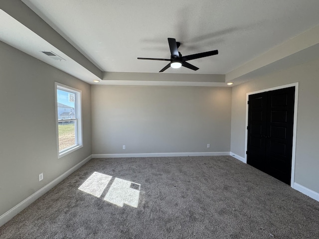 carpeted spare room featuring a raised ceiling, visible vents, baseboards, and ceiling fan