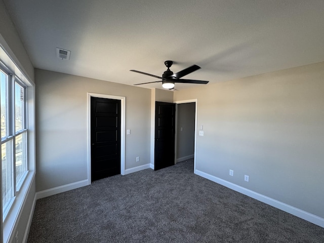 unfurnished bedroom with a ceiling fan, baseboards, visible vents, and dark colored carpet