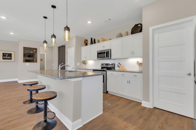 kitchen with a sink, appliances with stainless steel finishes, a breakfast bar area, light wood finished floors, and decorative backsplash