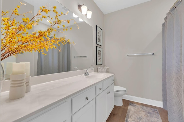 full bathroom featuring toilet, vanity, baseboards, and wood finished floors