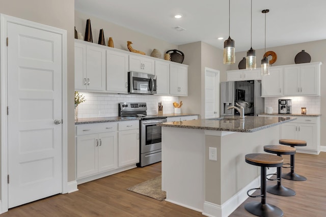 kitchen featuring white cabinets, light wood finished floors, an island with sink, and appliances with stainless steel finishes