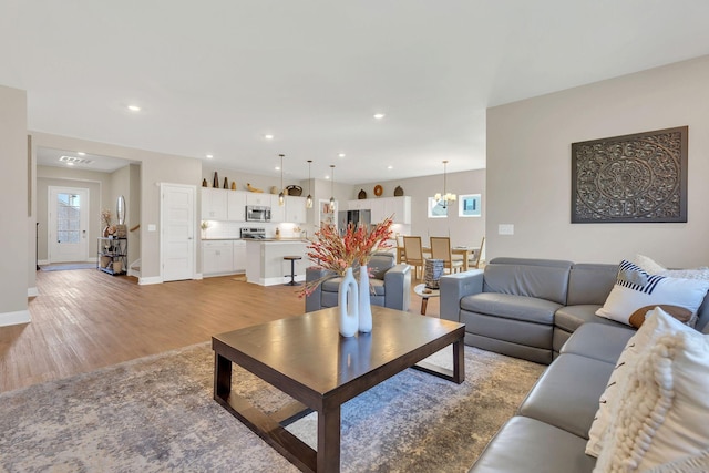 living area featuring a notable chandelier, recessed lighting, light wood-type flooring, and baseboards