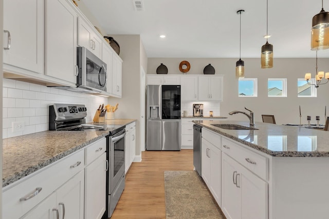 kitchen featuring pendant lighting, appliances with stainless steel finishes, light wood-style floors, white cabinetry, and a sink