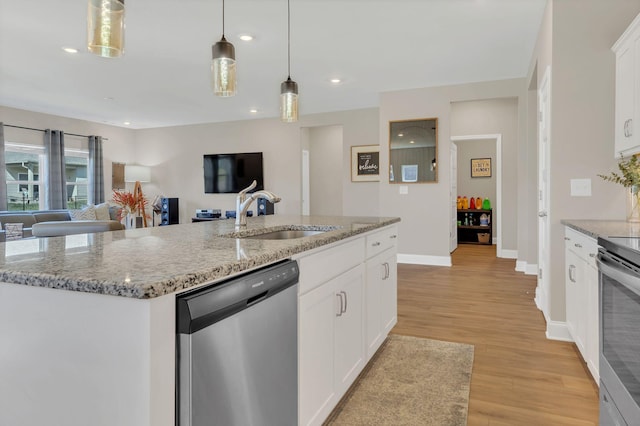 kitchen with a kitchen island with sink, a sink, decorative light fixtures, stainless steel appliances, and light wood-style floors