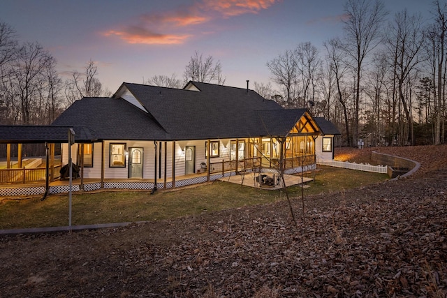 back of house at dusk with a deck, a lawn, and roof with shingles