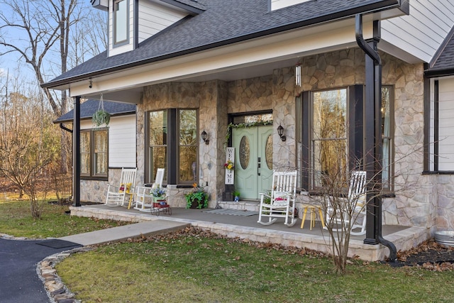 property entrance featuring stone siding, covered porch, and roof with shingles