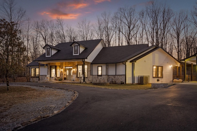 view of front facade with a shingled roof, stone siding, and curved driveway