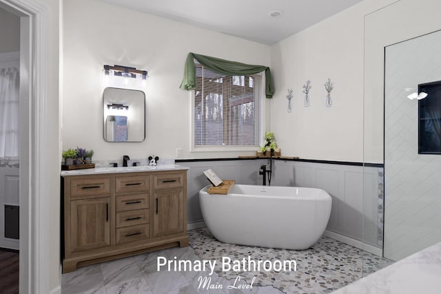 full bath with a freestanding tub, marble finish floor, wainscoting, and vanity