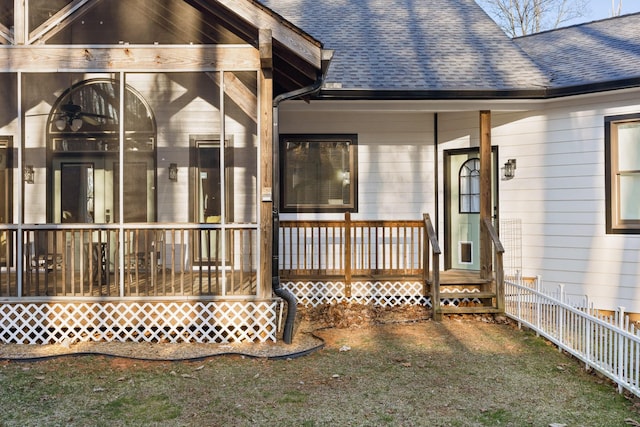 view of exterior entry featuring fence and a shingled roof