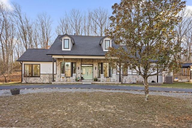 view of front of property featuring a porch, stone siding, and roof with shingles