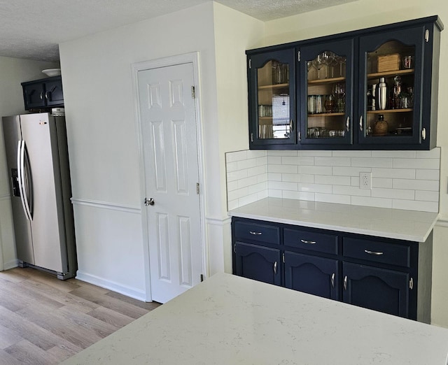 bar with tasteful backsplash, stainless steel fridge with ice dispenser, light wood-type flooring, and a textured ceiling