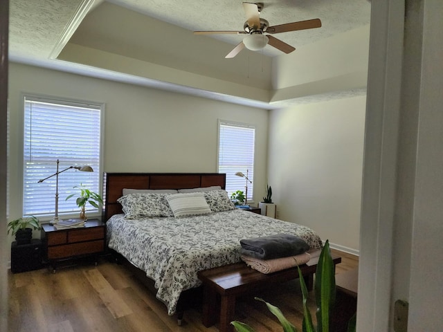 bedroom with a ceiling fan, a tray ceiling, wood finished floors, and a textured ceiling