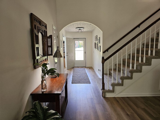 entryway featuring baseboards, arched walkways, wood finished floors, and stairs