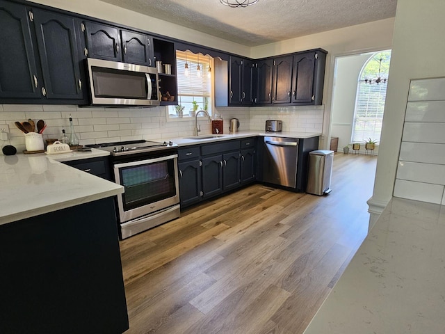 kitchen featuring light wood-style flooring, a sink, tasteful backsplash, stainless steel appliances, and light countertops