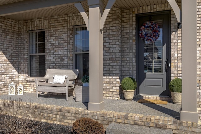 view of exterior entry with a porch and brick siding