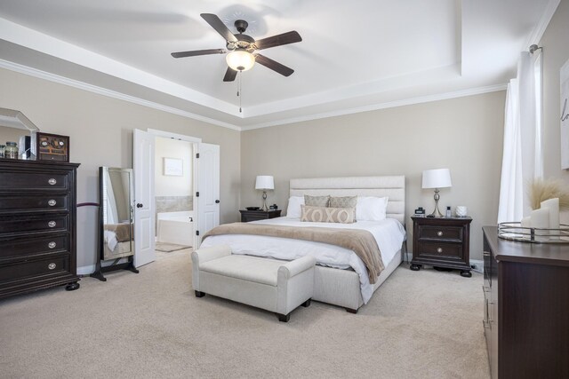 bedroom with a tray ceiling, light colored carpet, ensuite bath, and ornamental molding