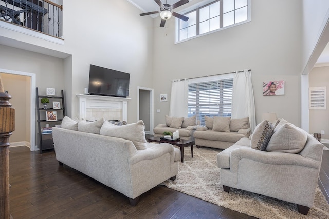 living room featuring a tiled fireplace, baseboards, a ceiling fan, and dark wood-style flooring