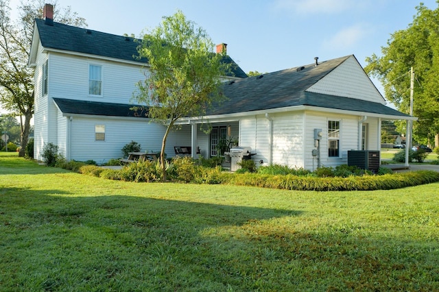 back of house featuring central AC unit, a chimney, and a yard