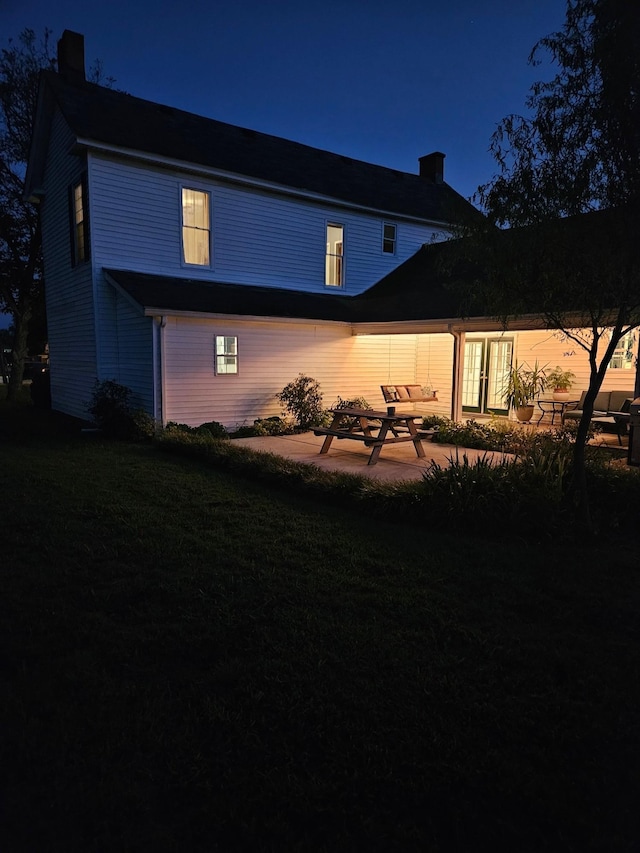 back of house at twilight with a lawn, a chimney, and a patio area