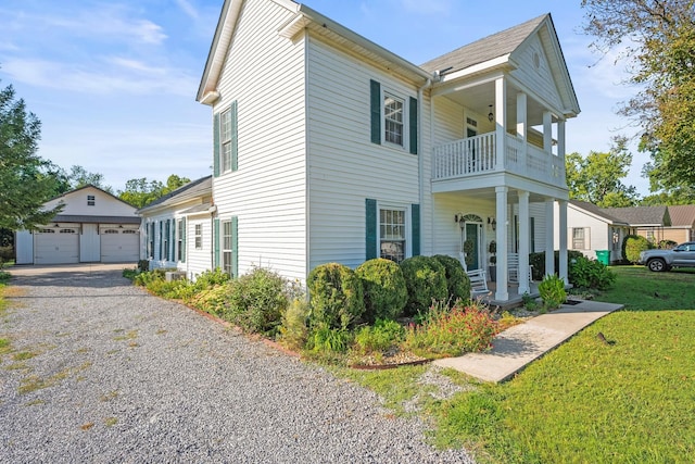 view of side of home featuring an outbuilding, a lawn, a detached garage, covered porch, and a balcony