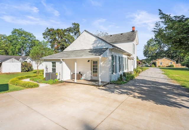 back of property with central AC unit, driveway, and a lawn