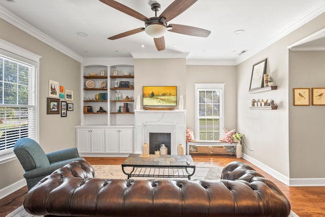 living room with built in shelves, crown molding, baseboards, a fireplace, and wood finished floors