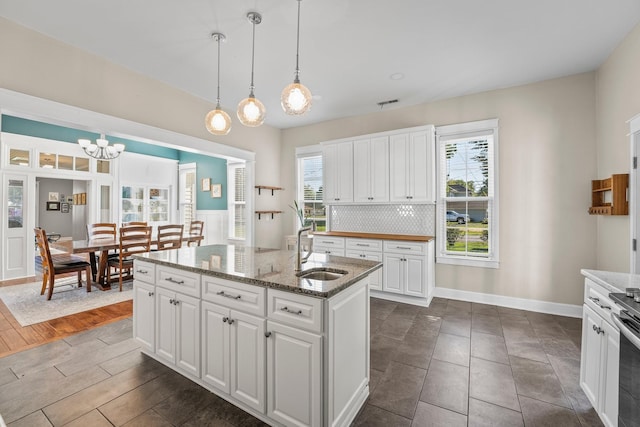 kitchen with pendant lighting, a kitchen island with sink, a sink, white cabinetry, and decorative backsplash