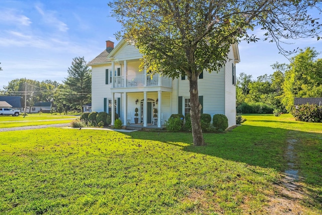 view of front of property featuring a front yard, a balcony, a porch, and a chimney