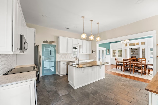 kitchen featuring pendant lighting, a kitchen bar, appliances with stainless steel finishes, white cabinets, and a kitchen island with sink