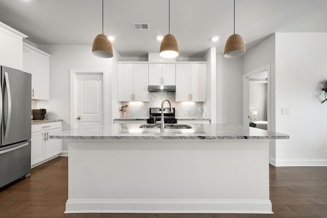 kitchen featuring tasteful backsplash, visible vents, under cabinet range hood, freestanding refrigerator, and a sink