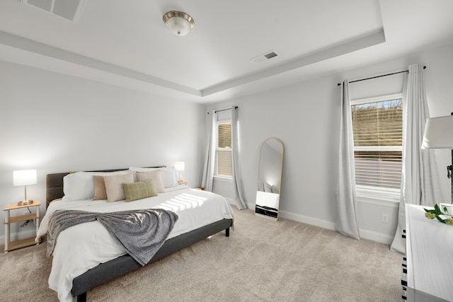 bedroom with visible vents, a raised ceiling, and light colored carpet