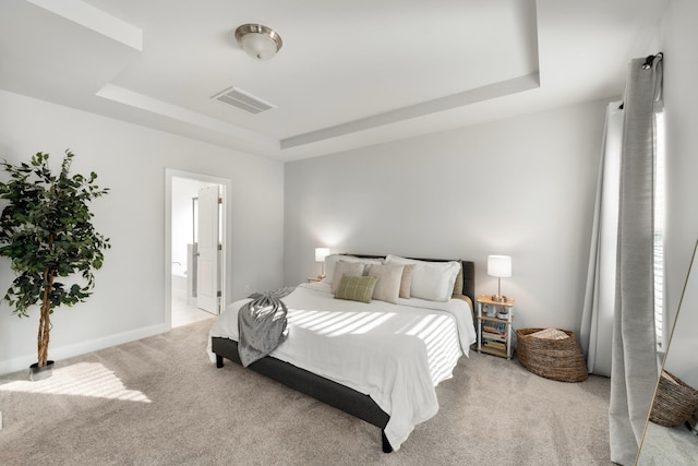 bedroom with visible vents, baseboards, a tray ceiling, light carpet, and ensuite bathroom