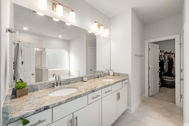 full bathroom featuring a walk in closet, double vanity, a stall shower, and a sink