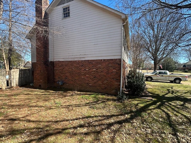 view of home's exterior with fence, brick siding, a chimney, and a lawn