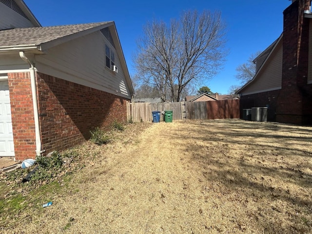 view of side of home featuring fence, cooling unit, a shingled roof, a garage, and brick siding