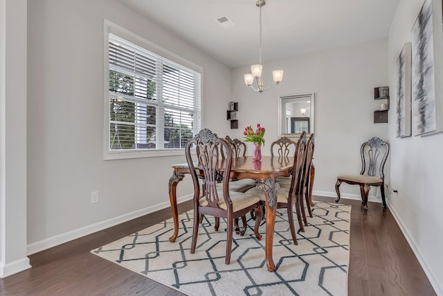 dining space with wood finished floors, visible vents, a chandelier, and baseboards