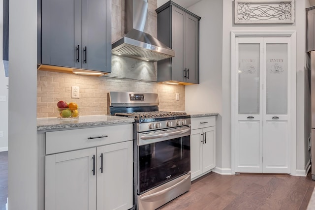 kitchen featuring light stone counters, decorative backsplash, wood finished floors, gas stove, and wall chimney exhaust hood