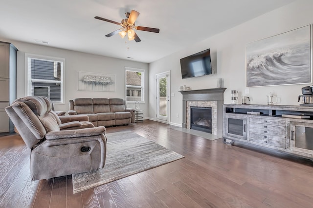 living area with a stone fireplace, wood finished floors, baseboards, and a ceiling fan