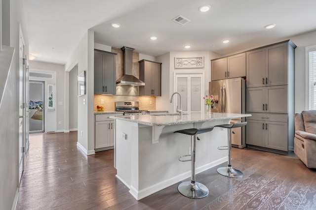 kitchen featuring visible vents, a sink, a kitchen breakfast bar, stainless steel appliances, and wall chimney exhaust hood