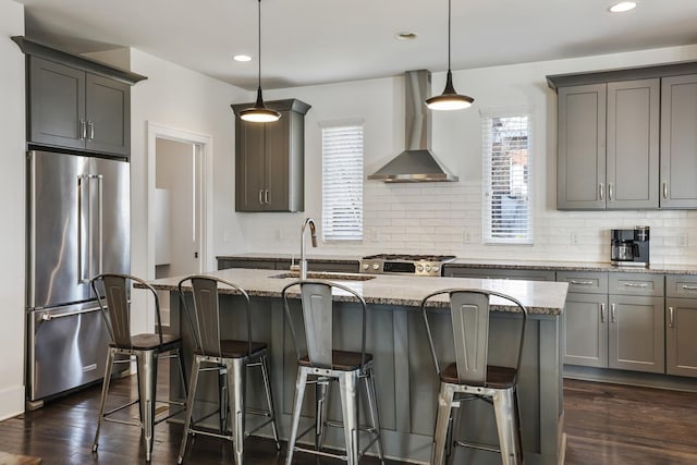 kitchen featuring a sink, decorative backsplash, stove, high end refrigerator, and wall chimney range hood