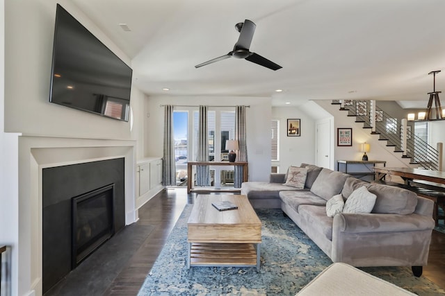 living room with a fireplace with flush hearth, ceiling fan with notable chandelier, recessed lighting, stairway, and dark wood-style flooring