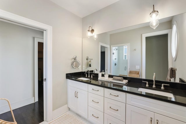 bathroom featuring double vanity, a stall shower, baseboards, and a sink