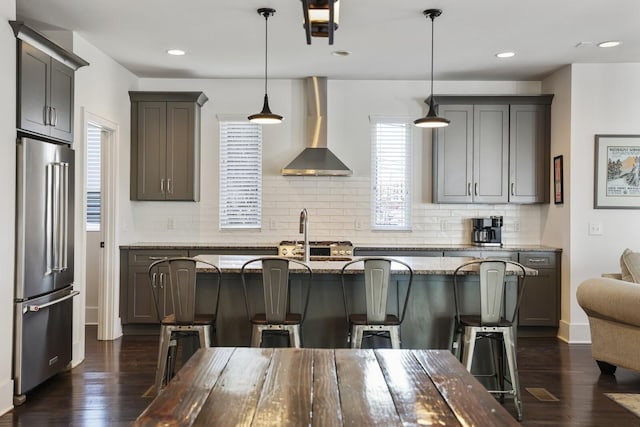 kitchen with tasteful backsplash, a breakfast bar, high quality fridge, dark wood-style floors, and wall chimney exhaust hood