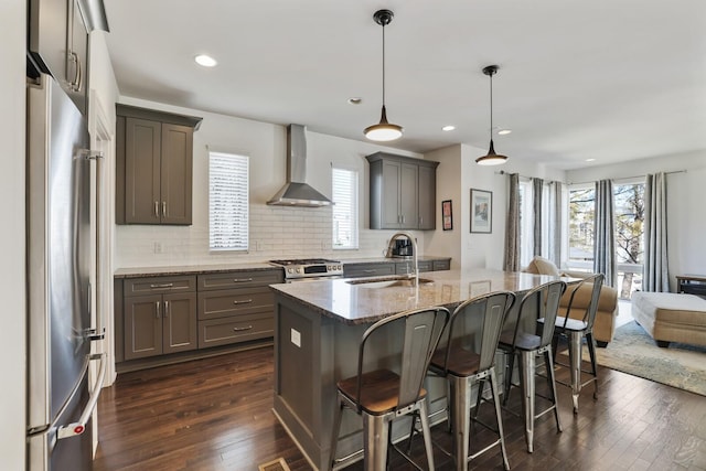 kitchen with gray cabinetry, wall chimney range hood, dark wood-style floors, stainless steel appliances, and a sink