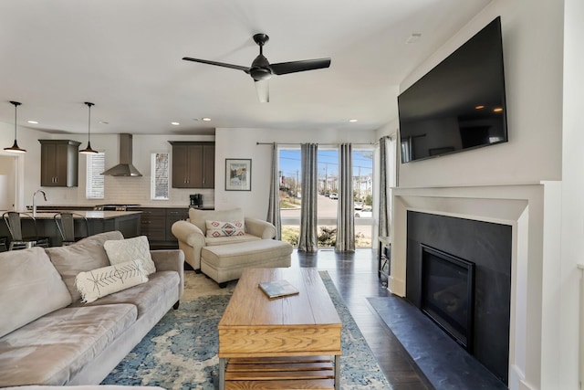 living room with plenty of natural light, a ceiling fan, a glass covered fireplace, and dark wood finished floors