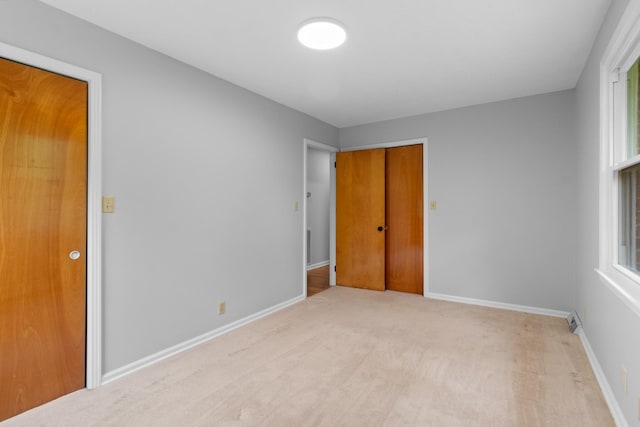 unfurnished bedroom featuring multiple windows, light colored carpet, baseboards, and a closet