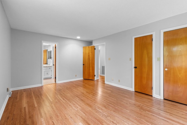 unfurnished bedroom featuring light wood-style flooring, visible vents, baseboards, and ensuite bathroom