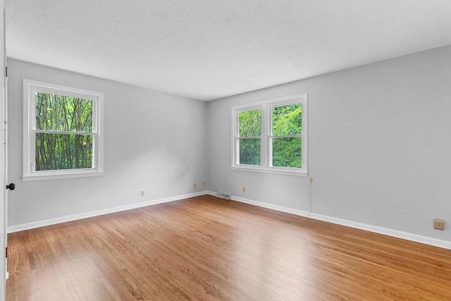 empty room with a wealth of natural light, visible vents, baseboards, and wood finished floors